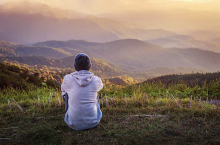 Hombre joven que se sienta solo al aire libre con las montañas en fondo en la mañana.